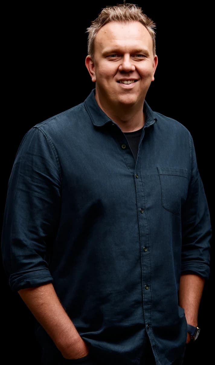 Maximilian Braig, persönlicher Ansprechpartner für professionelle SEO-Beratung, lächelt freundlich in die Kamera. Freigestelltes Porträt im dunklen Hemd, locker mit den Händen in den Hosentaschen.