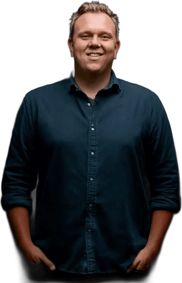 Maximilian Braig, persönlicher Ansprechpartner für Website, SEO und GEO, lächelt vor dunklem Hintergrund. Dunkelblaues Hemd, hochgekrempelte Ärmel, nahbarer und kompetenter Ausdruck. Warmes Studiolicht schafft eine vertrauensvolle Atmosphäre.